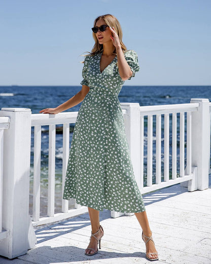 Woman in a green floral dress standing on a deck by the ocean.