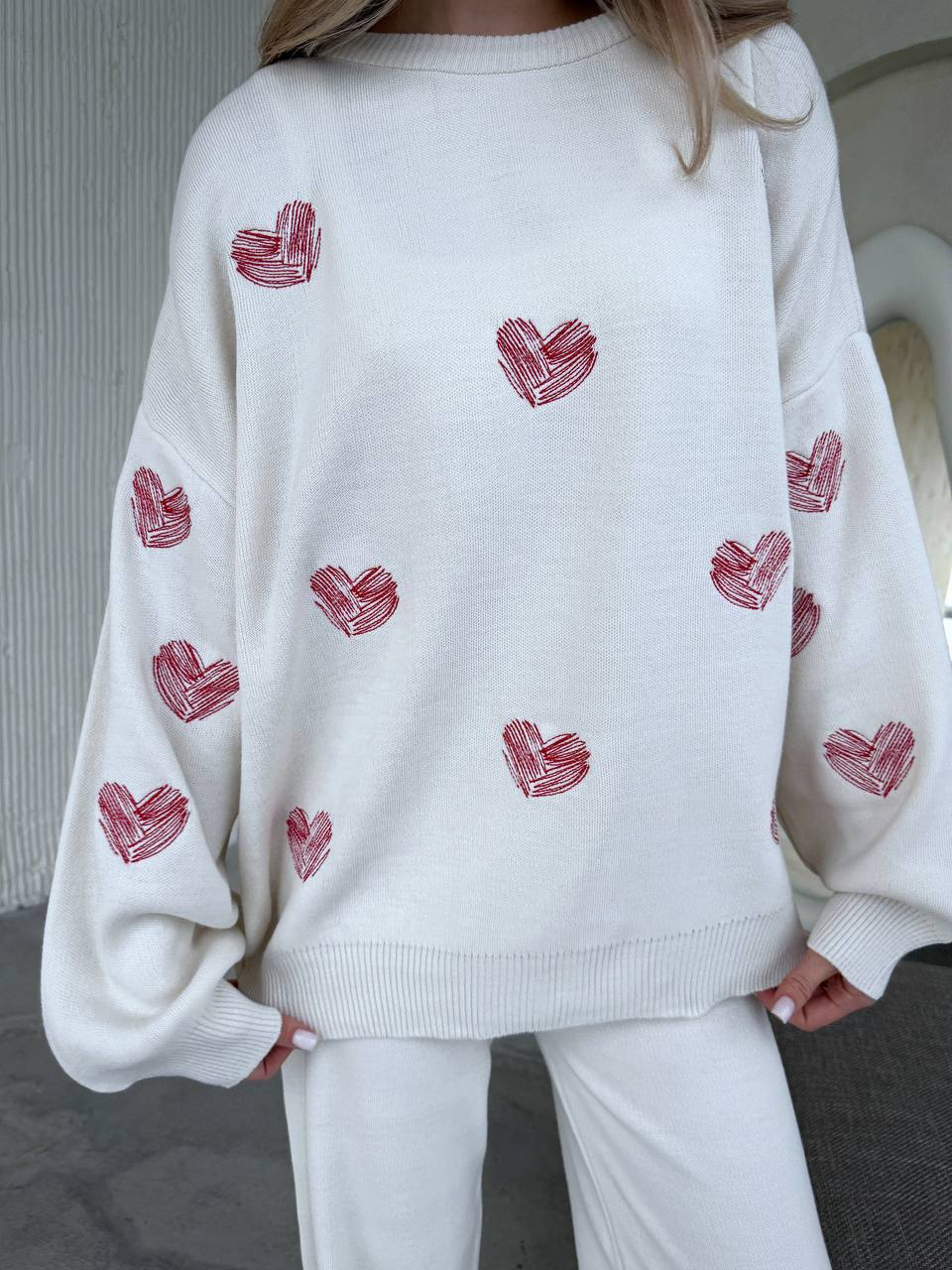 White sweater with red heart patterns worn by a person indoors.