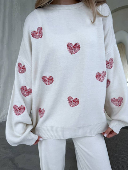 White sweater with red heart patterns worn by a person indoors.
