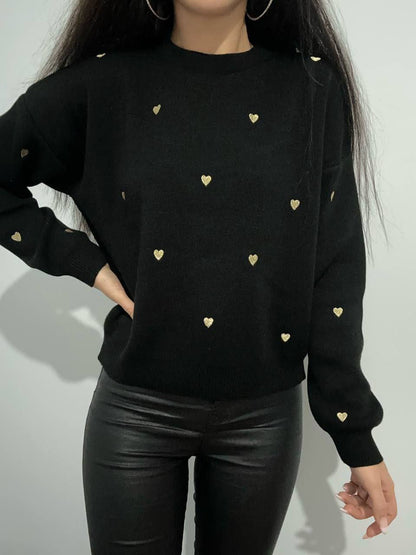 Black sweater with gold heart patterns worn by a person on a plain background