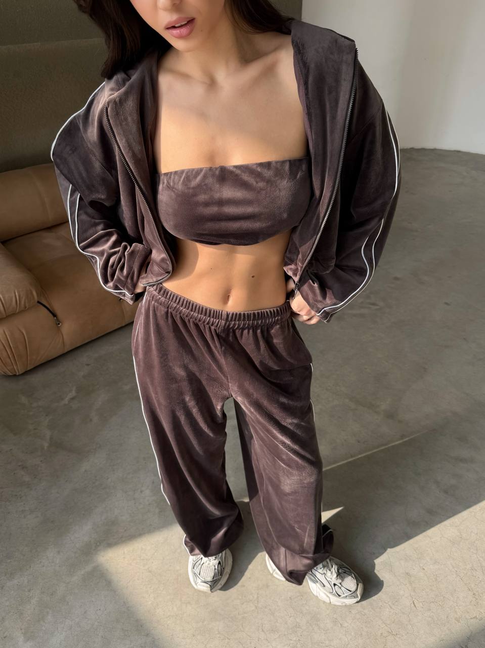 Person wearing a brown velour tracksuit in a room with a beige couch.