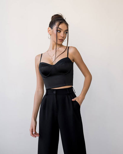 Woman wearing a black crop top and high-waisted pants against a plain background