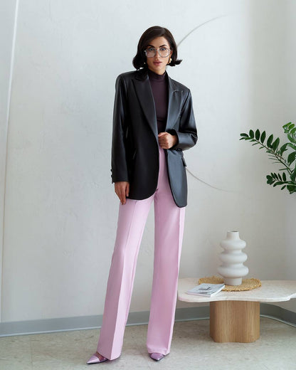 Woman in a black blazer and pink pants standing in a modern interior setting.