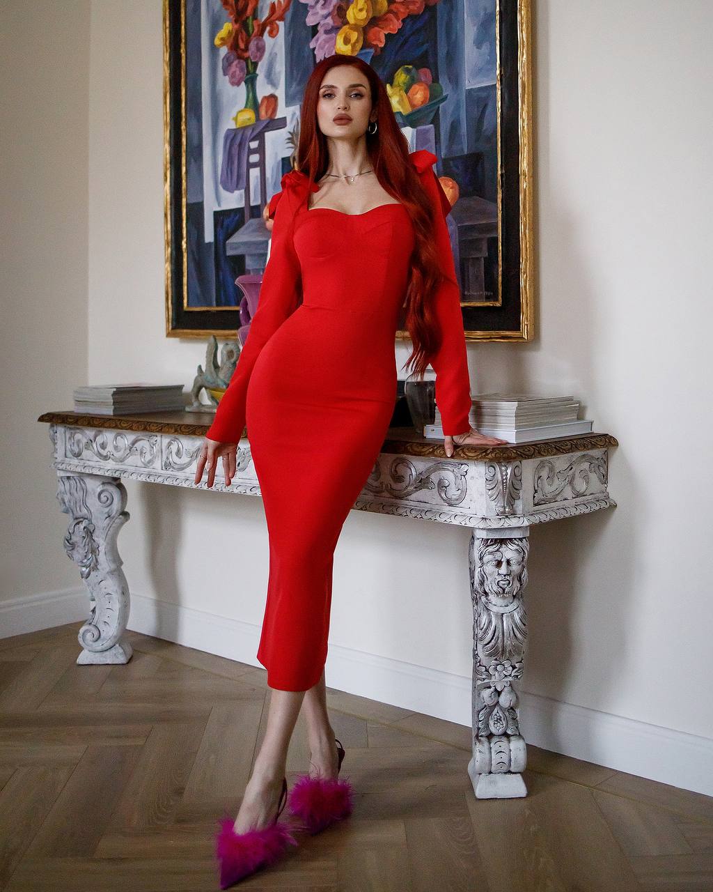 Woman in a red dress standing on a decorative table with a colorful painting in the background
