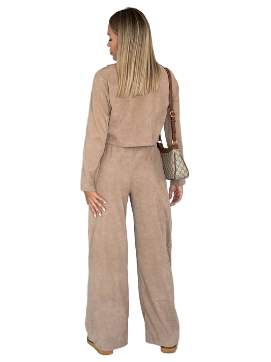 Woman wearing a beige outfit with wide-leg pants and a matching jacket, carrying a brown handbag on a white background.