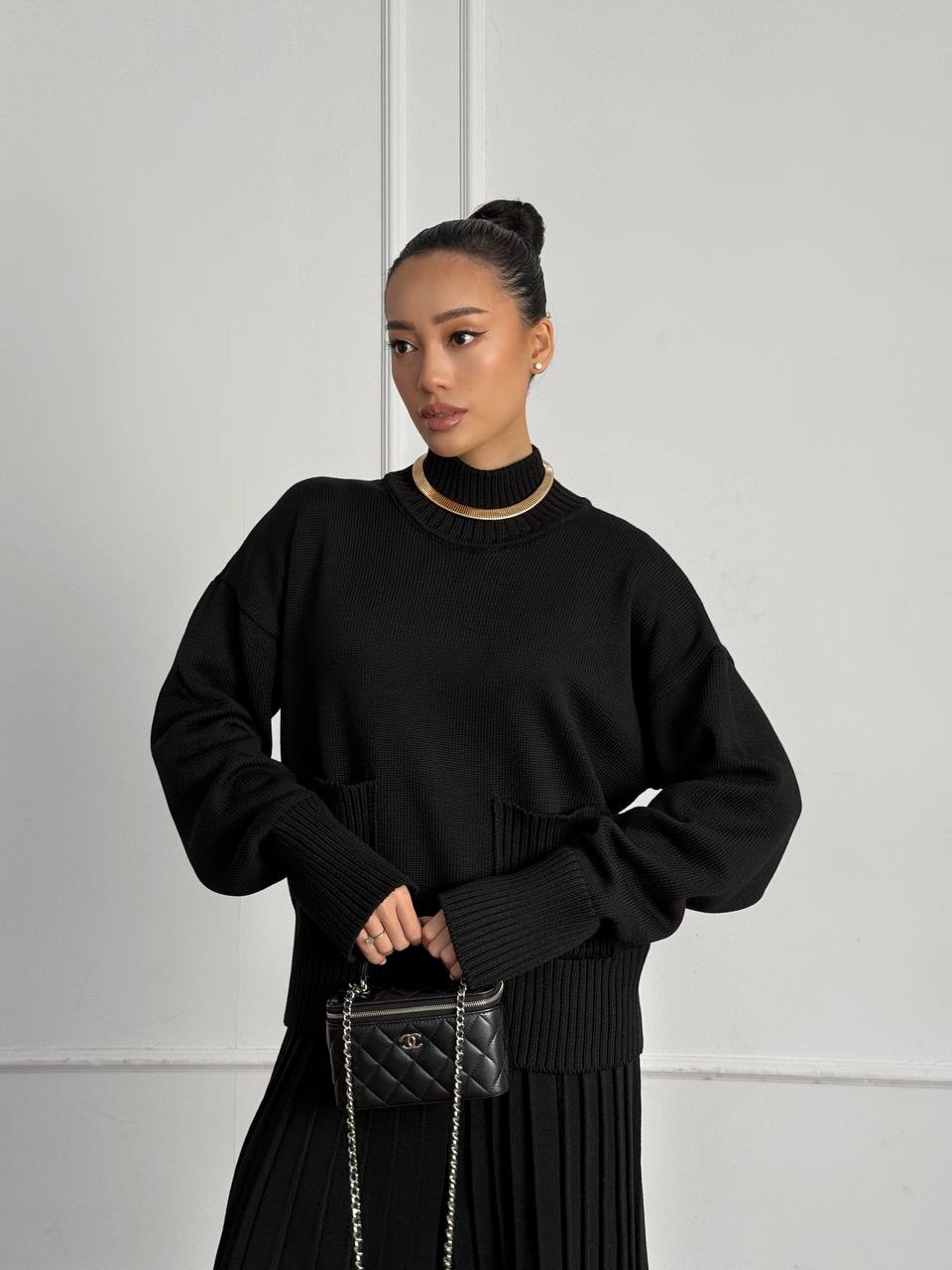 Woman wearing a black outfit holding a handbag against a plain background