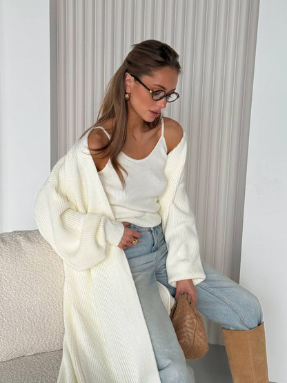 Woman wearing a white cardigan, white top, and light blue jeans sitting on a couch.