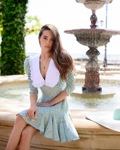 Woman in a light blue dress with white collar sitting by a fountain