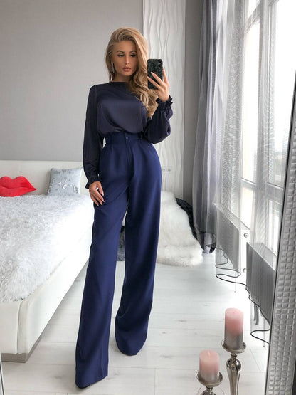 Woman taking a mirror selfie wearing a navy blue jumpsuit in a bedroom.
