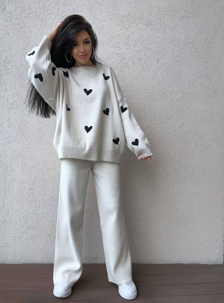Person wearing a white outfit with black heart patterns against a plain background