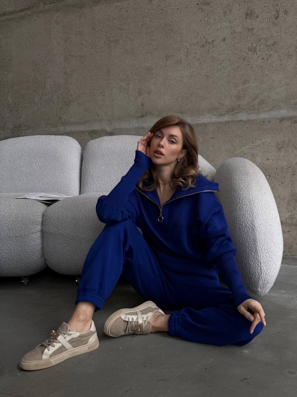 Woman in a blue tracksuit sitting on a modern chair against a concrete wall.