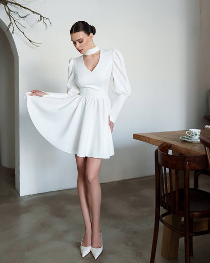 Woman in a white dress standing in a room with wooden furniture.
