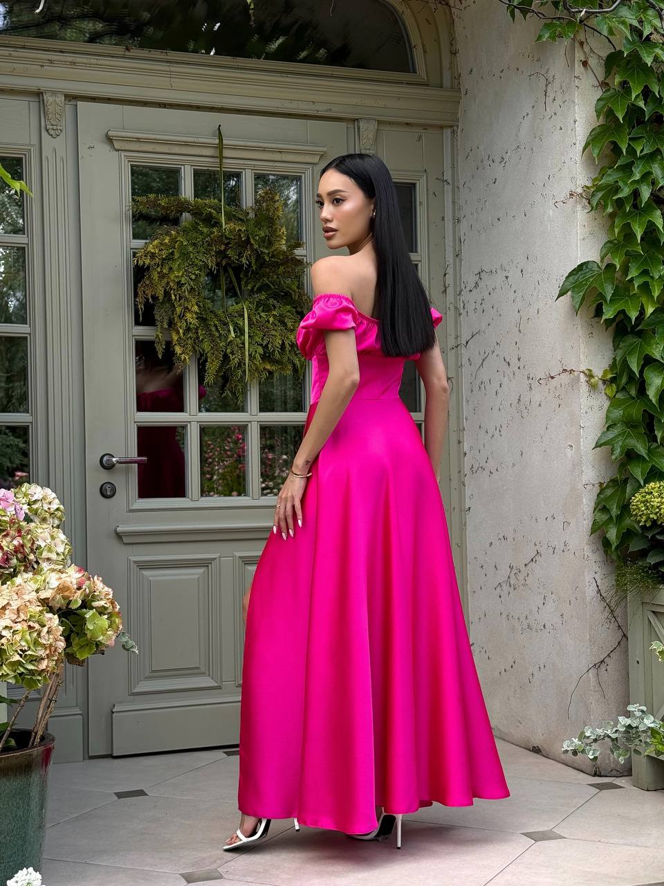 Woman in a bright pink off-shoulder gown standing in front of a door with plants.