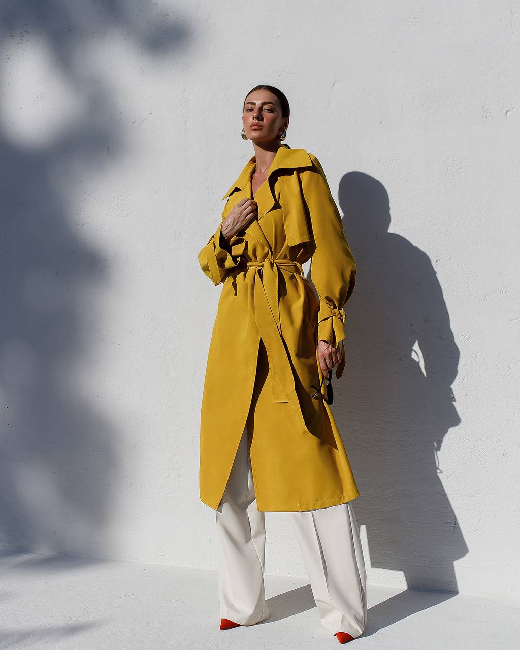 Person wearing a yellow trench coat against a white wall