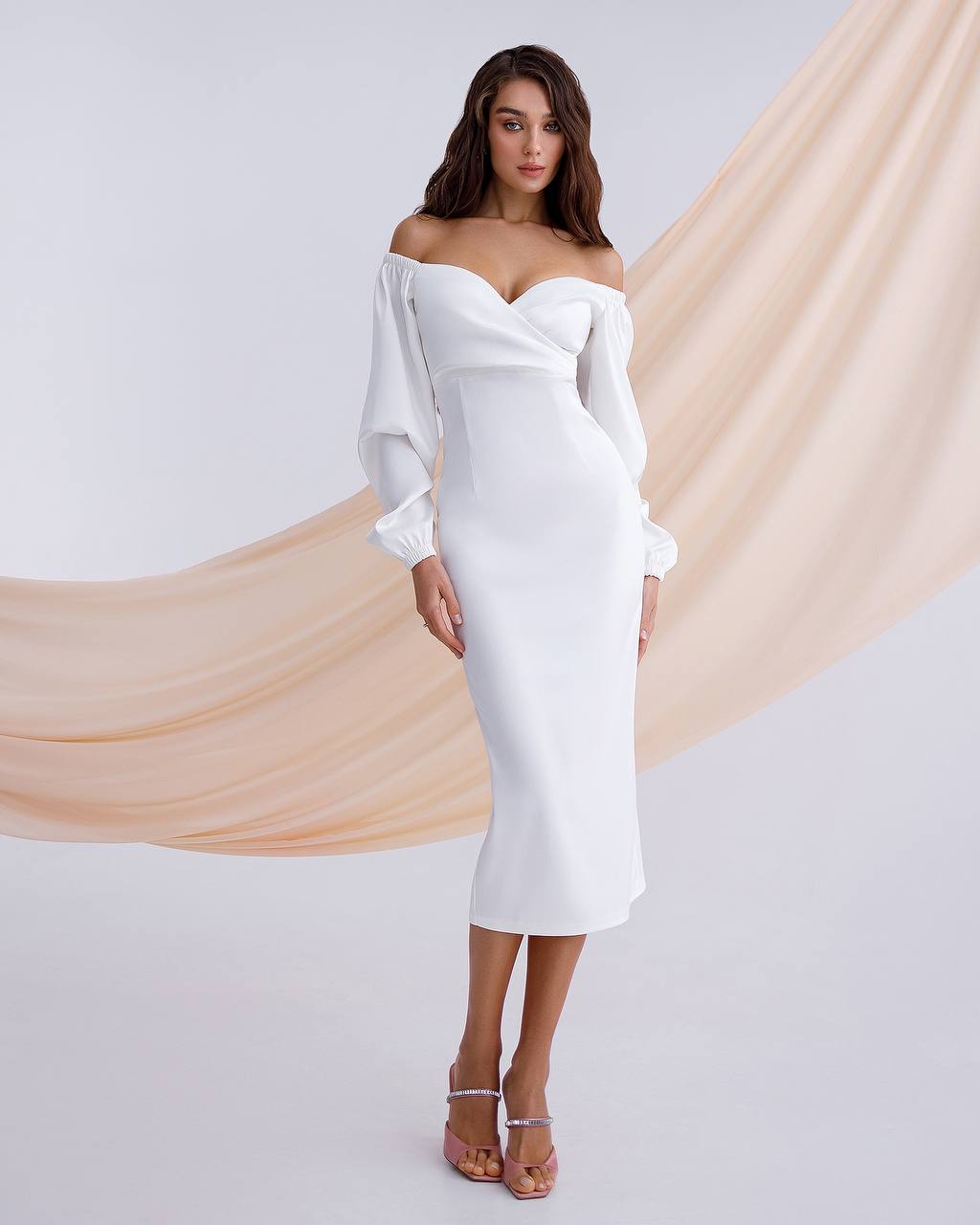 Woman wearing a white off-shoulder dress with long sleeves against a plain background