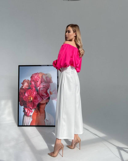 Woman in a bright pink top and white pants standing next to a framed floral artwork.