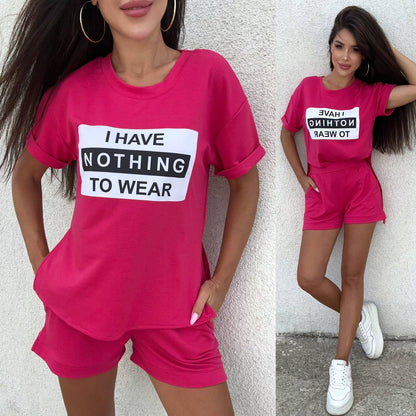 Woman wearing a pink outfit with a 'I HAVE NOTHING TO WEAR' t-shirt against a light gray wall.
