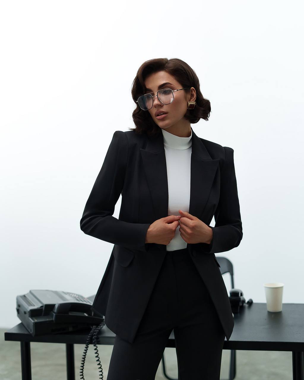 Woman in a black suit standing in an office setting with a white background