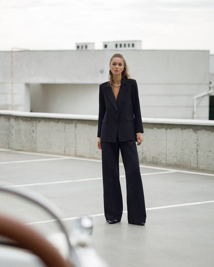 Woman in a black suit standing on a rooftop with a neutral background