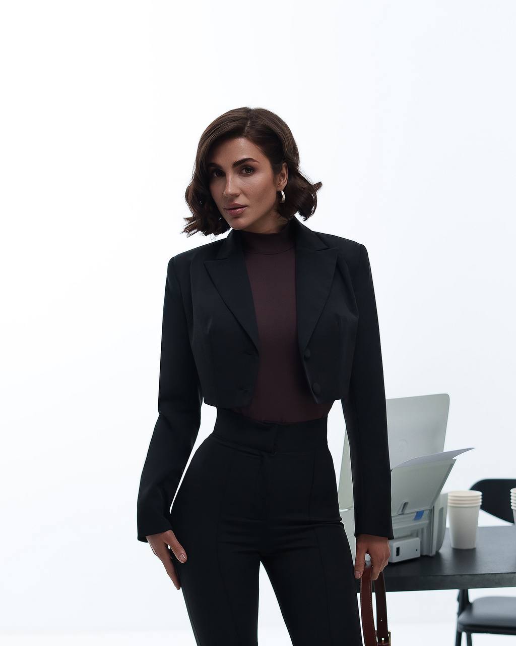 Woman in a black suit standing in an office setting with a white background