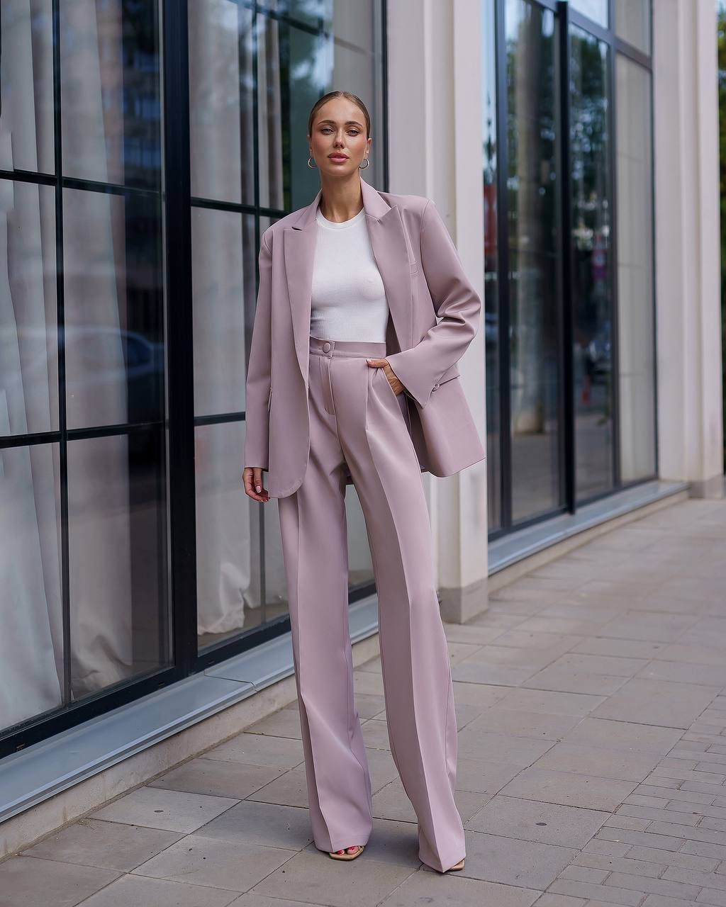 Woman in a pink suit standing outside a building with large windows.