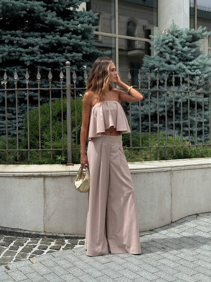 Woman in a light pink outfit standing outdoors with greenery in the background