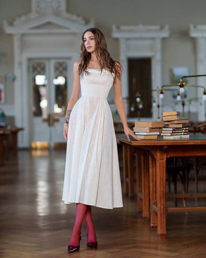 Woman in a white dress standing in a room with wooden tables and books.
