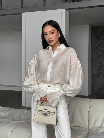 Woman in a white outfit holding a beige handbag in a minimalistic room.