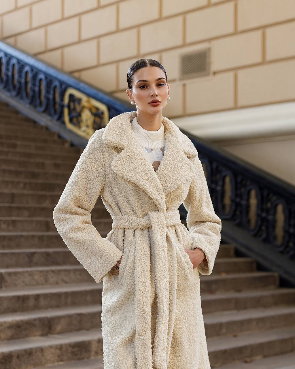 Woman wearing a beige coat standing on steps with a building in the background