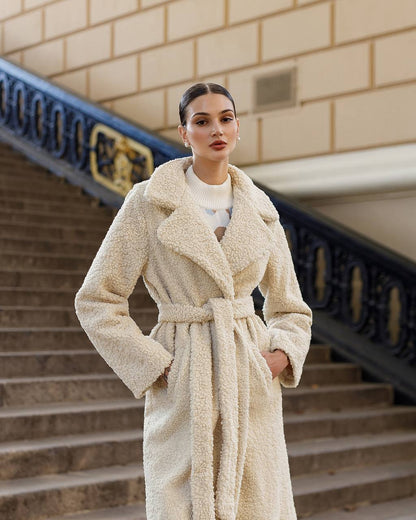 Woman wearing a beige coat standing on steps with a building in the background
