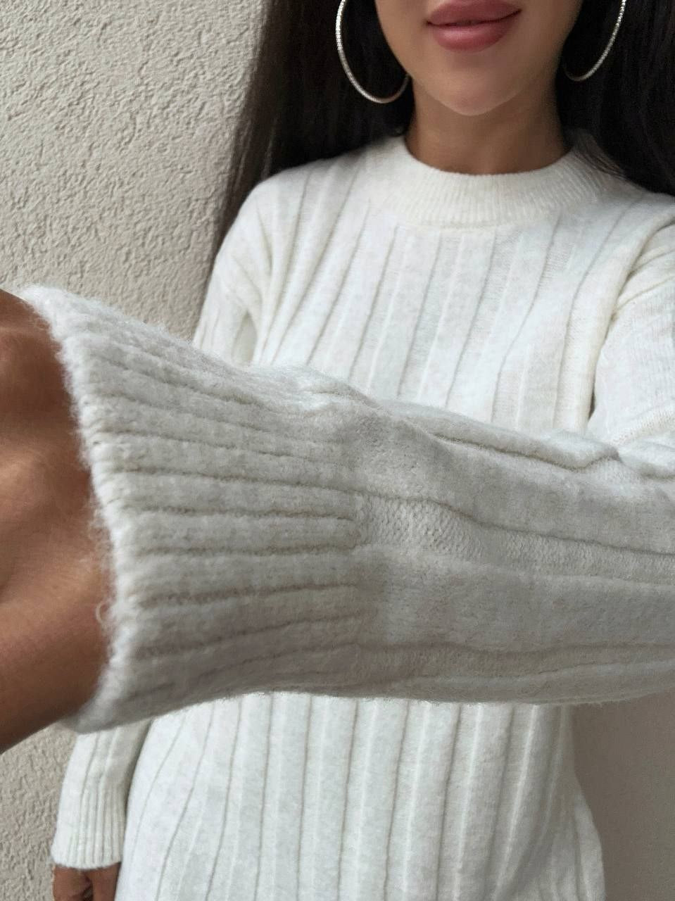 Person wearing a white ribbed sweater with a neutral background