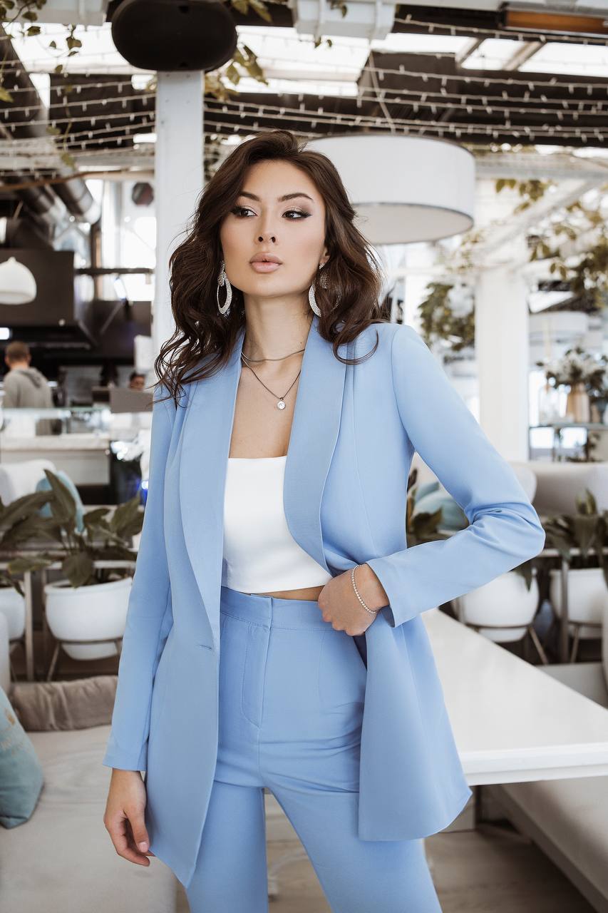 Woman in a light blue suit standing in an indoor setting with tables and chairs.