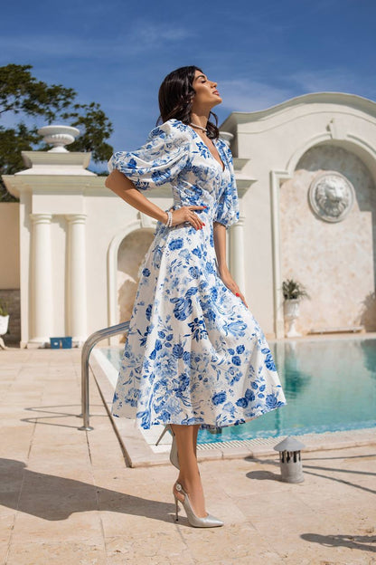 Woman in a blue floral dress standing by a pool with classical architecture in the background