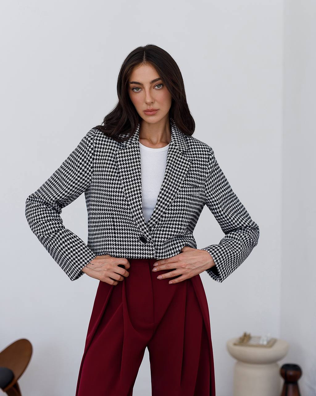 Woman wearing a black and white checkered jacket and red pants against a plain background