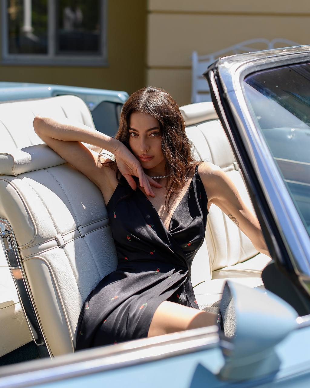 Woman sitting in the back seat of a convertible car with a neutral background