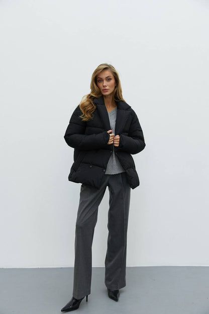 Woman wearing a black coat and gray pants against a white background