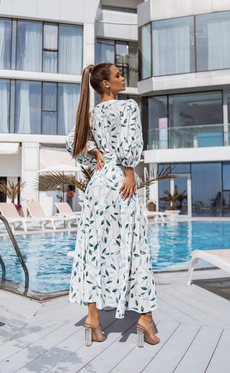 Woman in a white dress with green patterns standing by a poolside.