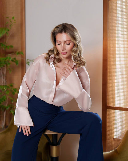 Woman wearing a light pink blouse and blue pants sitting on a stool indoors.