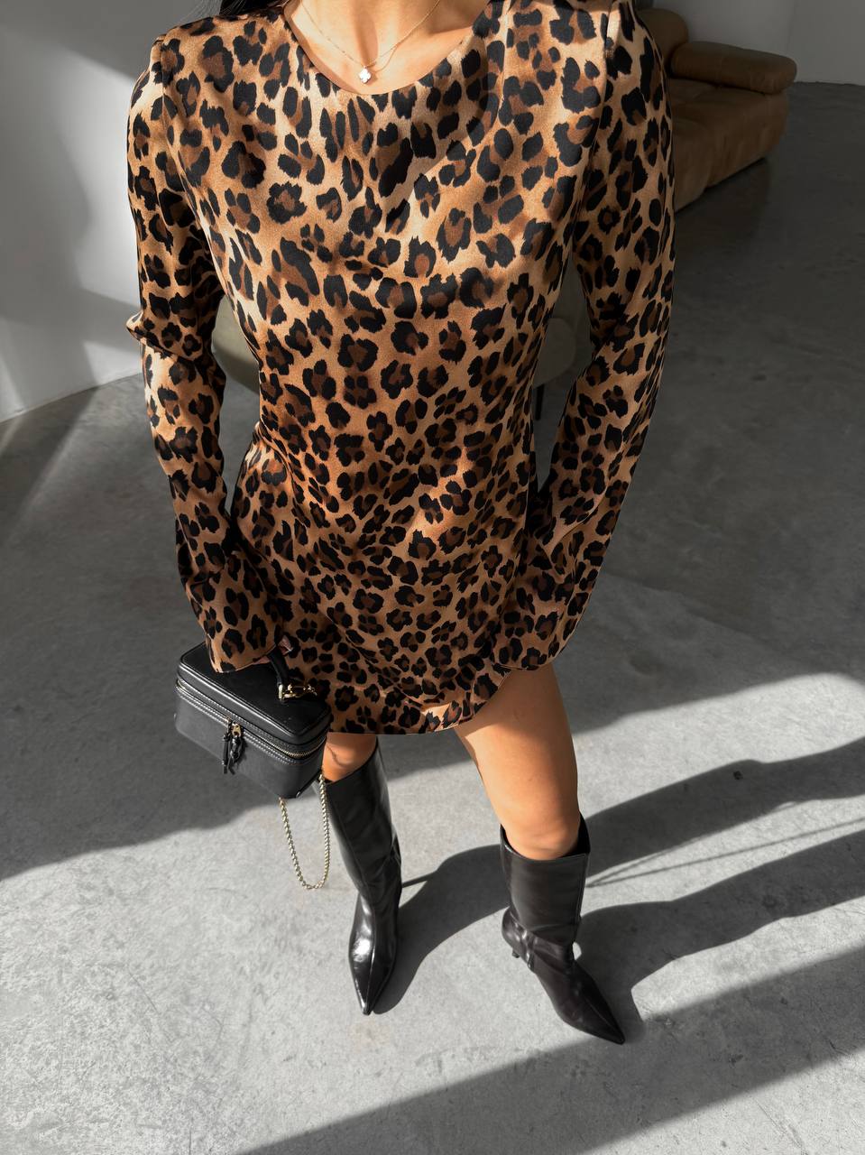 Person wearing a leopard print dress with black boots on a light gray floor.
