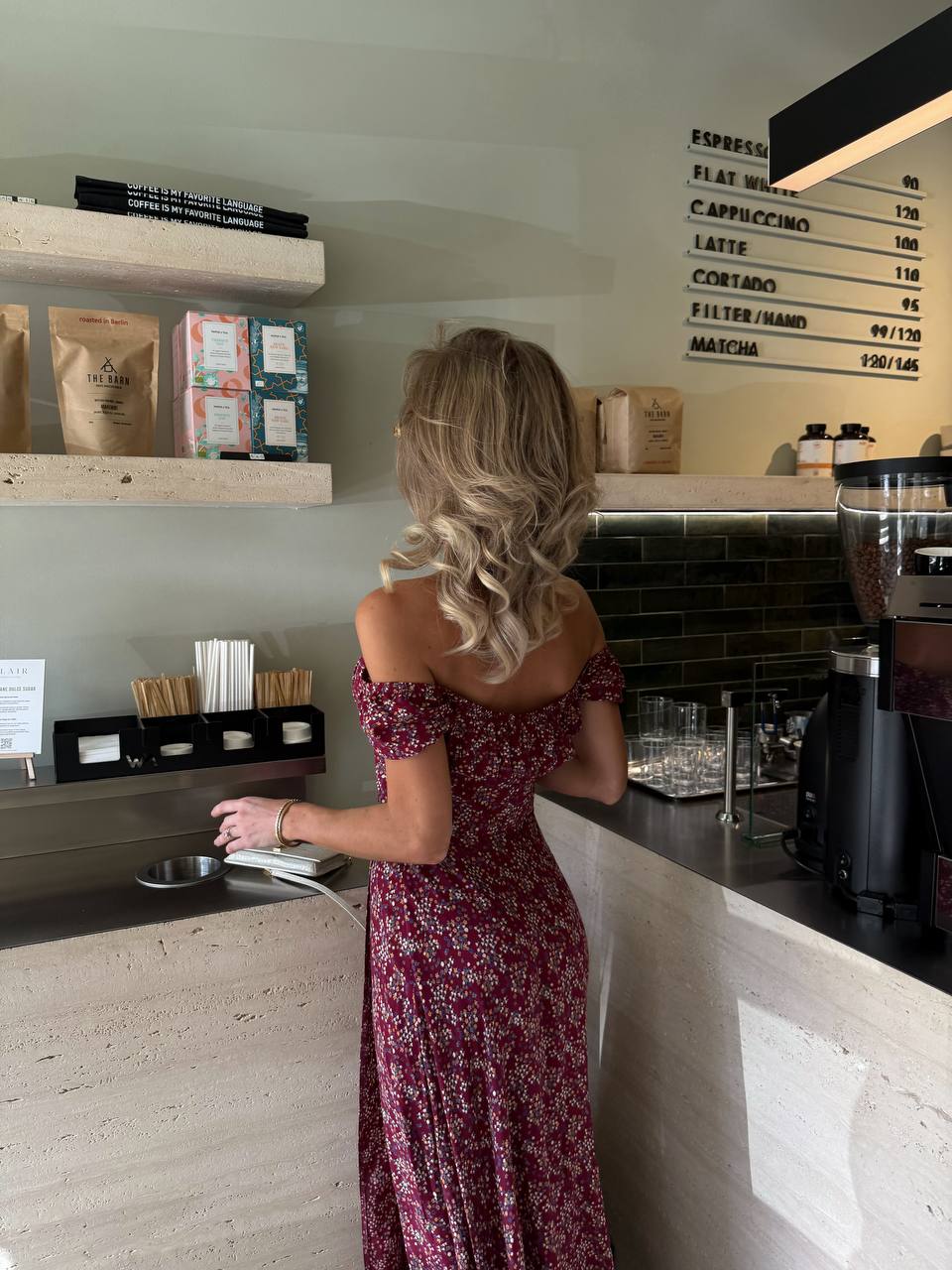 Woman in a floral dress standing at a counter in a coffee shop.