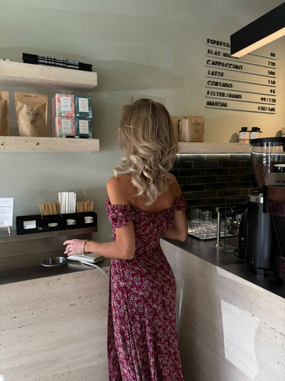 Woman in a floral dress standing at a counter in a coffee shop.