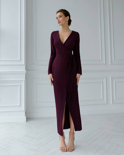 Woman wearing a burgundy long-sleeve dress with a slit in a white room.