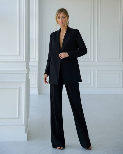 Woman wearing a black suit standing against a white paneled wall.