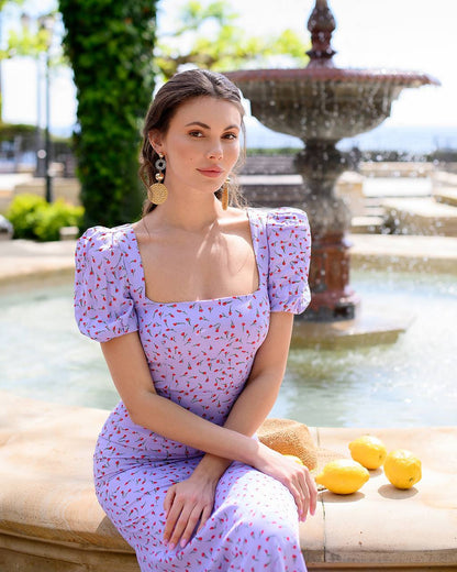 Woman in a light purple dress sitting by a fountain with lemons on a stone ledge.