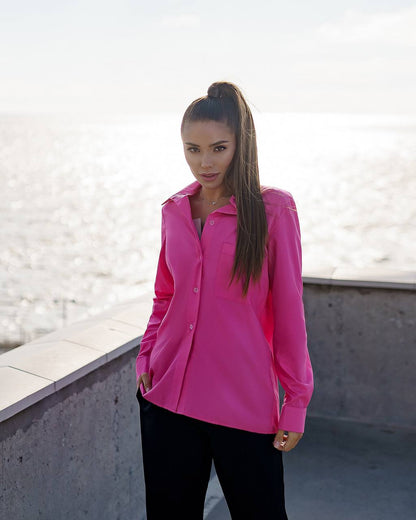 Woman wearing a bright pink shirt standing on a rooftop with a light background