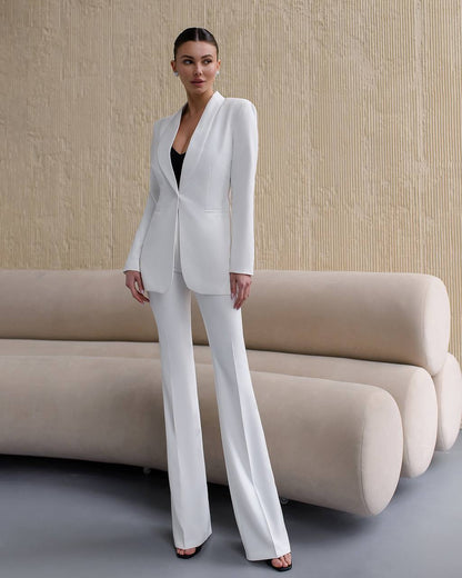 Woman in a white suit standing in a modern interior setting with a beige sofa.