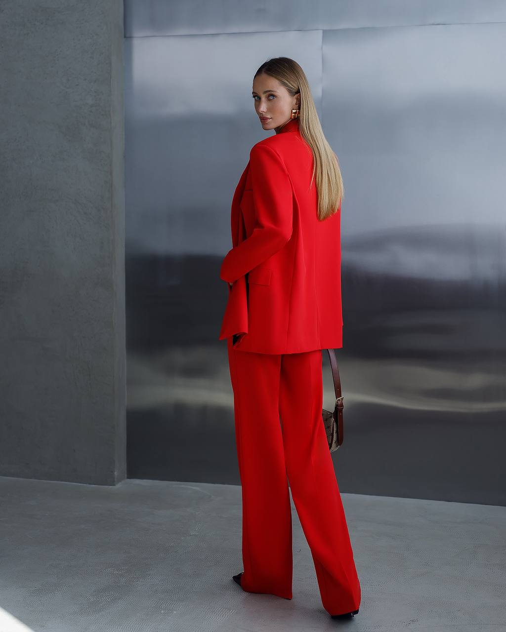 Woman in a red suit standing against a gray wall