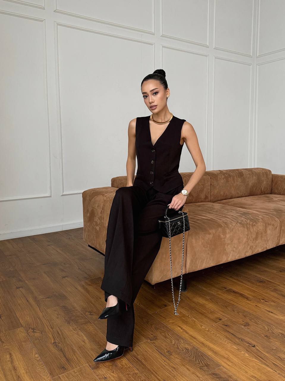 Woman in a black outfit sitting on a brown sofa in a room with white paneled walls.