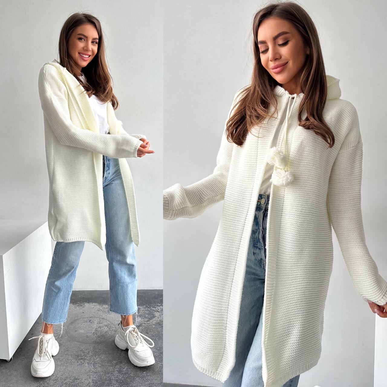 Woman wearing a long cream cardigan over a white top with blue jeans and white sneakers, standing against a plain background.