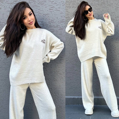 Woman wearing a white sweater and pants set against a gray wall.